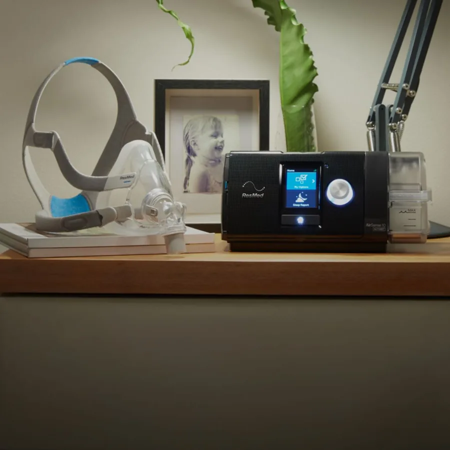 A CPAP machine with humidifier and a full face mask on a bedside table
